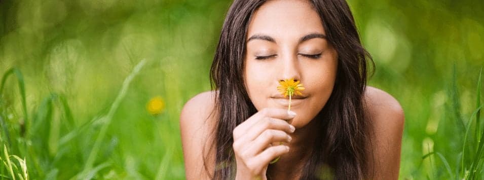 woman smelling flower in grassy field